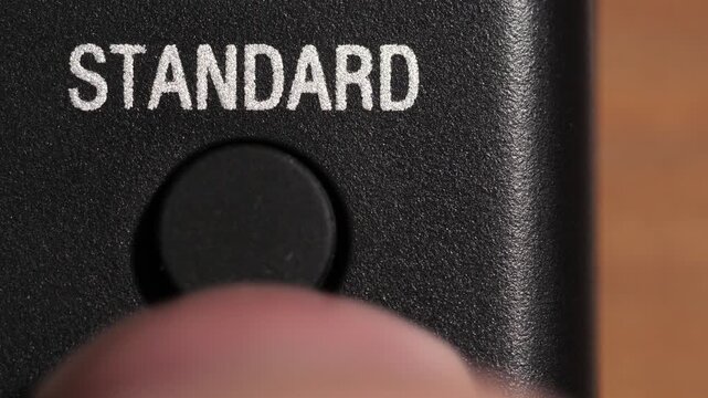 Finger presses black standard button below white text on textured black remote