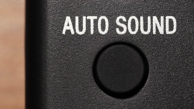 Macro view of finger pressing black auto sound button below white text on black panel