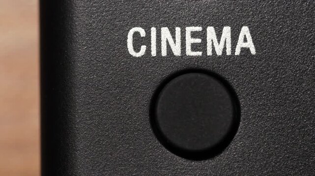 Macro view of finger pressing black cinema button below white text on black panel
