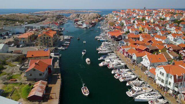Aerial drone flyover above Sm&ouml;gen channel in Bohusl&auml;n Sweden with boats cruising between colorful coastal houses lining both sides toward open sea