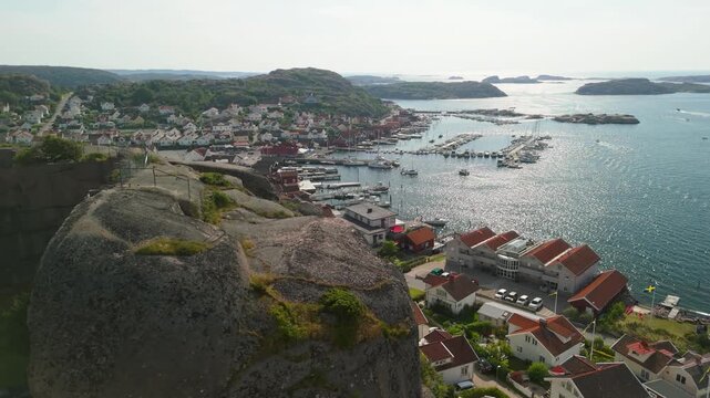 Drone parallax shot reveals Bovallstrand coastal town in Bohusl&auml;n, Sweden, with granite cliffs, red-roofed houses, marina and scenic archipelago