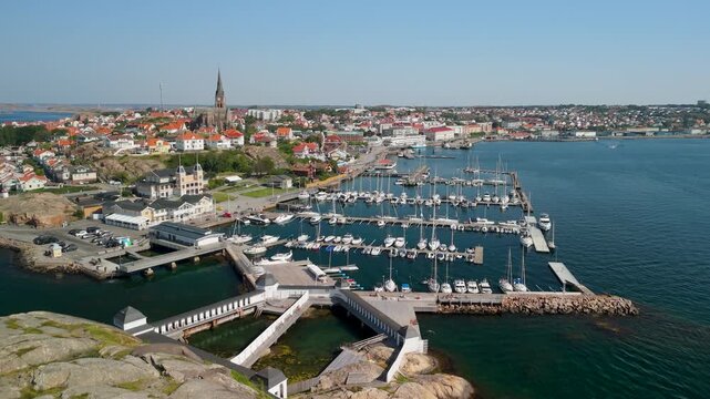 Aerial pull back from Lysekil marina in Bohusl&auml;n Sweden revealing rows of sailboats historic bathhouse church spire and coastal cityscape along open sea