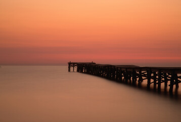 Fototapeta premium Wooden jetty at sunset in Alcudia Bay, Mallorca, Spain. Long exposure of Playa de Muro beach, minimalist zen concept with calm water and negative space