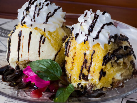 Traditional Hungarian Soml&oacute;i galuska dessert served on a glass plate with whipped cream and chocolate sauce. Close-up view of sponge cake trifle scoops drizzled with dark chocolate syrup.