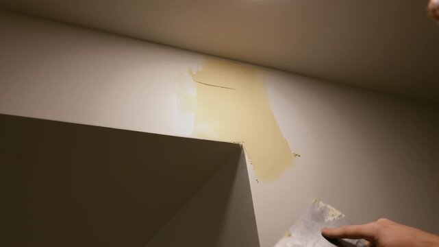 Close up view of Worker applying wall putty with a spatula to repair surface imperfections. Interior renovation process showing smoothing and preparation of wall before painting in a home improvement