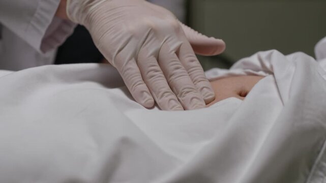 Doctor's gloved hand gently palpating patient's abdomen for medical examination