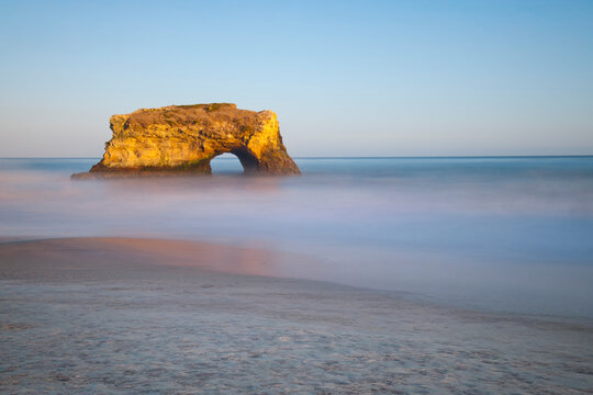 Natural Rock Arch at Santa Cruz Seaside with Motion Blur Waves and Clear Blue Sky