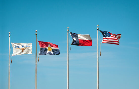 Fort Worth, Dallas, Texas state flags and American flag waving in the wind on flag poles. Blue sky background with copy space. 