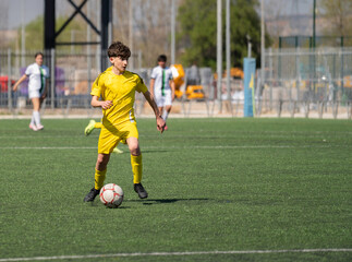 Fototapeta premium Young male athlete in yellow jersey playing soccer on artificial turf pitch during game with copy space