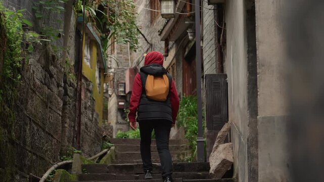 White backpacker ascending mossy stone steps in narrow historic alley, wearing red jacket and yellow backpack, passing weathered stone walls covered with ivy, quiet morning atmosphere, cinematic