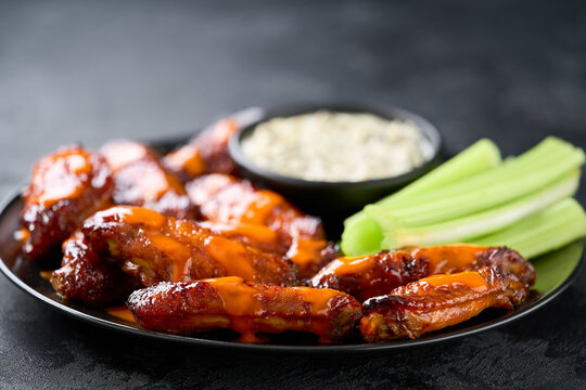 crunchy buffalo chicken wings with celery sticks and blue cheese dipping sauce on a dark table.