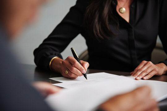 Professional businesswoman signing an important document with a pen at a dark desk in a modern office
