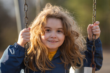 Child laughing on swing in playground. Kid smiling portrait outdoors in park. Carefree child...