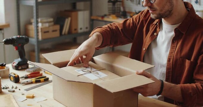 Man packaging parcel inside workshop studio with craft tools