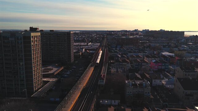 An aerial view over the elevated subway A line running through Rockaway Park on a sunny morning. The drone camera dolly in towards a train waiting at the station.