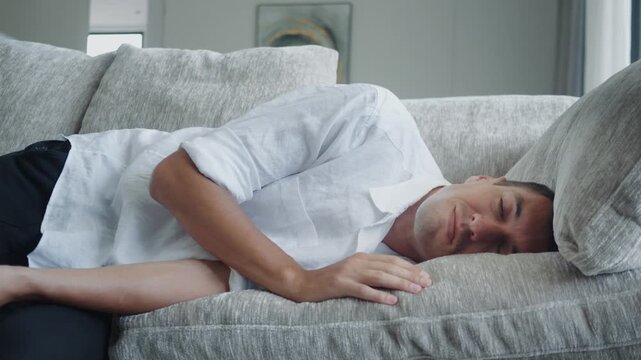 Burnout concept. Extremely tired businessman collapses on couch after stressful workday. Exhausted man lying on sofa with empty look showing work stress burnout fatigue and lack of energy at home.