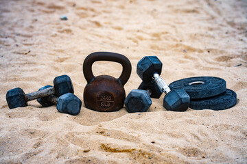 Sport kettlebell training. Sport dumbbells on sand. Sporty outdoor fitness. Sport weightlifting...