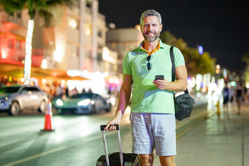 Traveler using phone in Miami streets at night. Traveler call phone during his summer trip....