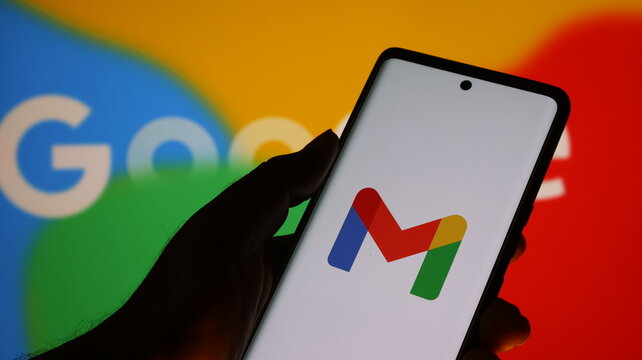A hand holding a smartphone with the gmail logo on the screen in front of a google logo background