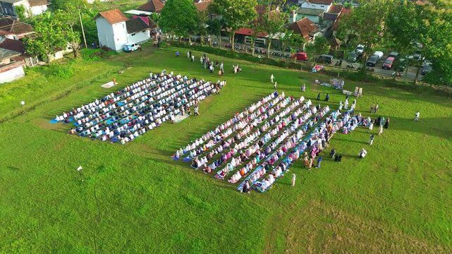 Outdoor congregation for Eid prayer, rows of Muslims aligned neatly on a green open space.
