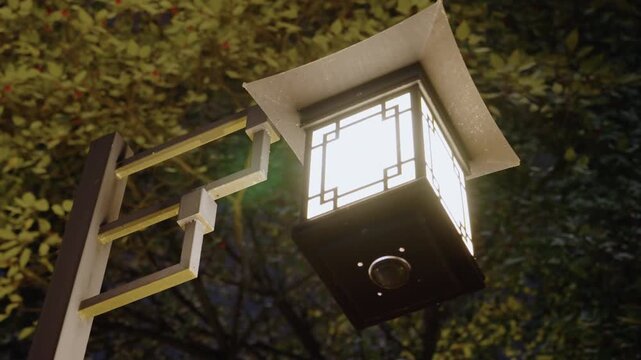Glowing lantern hanging on wooden post under leafy canopy at dusk, japaneseinspired square fixture casts warm soft light, metal bracket and decorative frame visible, gentle bokeh and shadow play