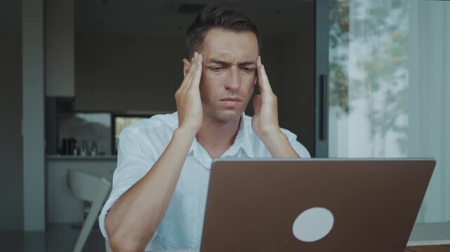 Stress and headache overwhelm tired businessman working on laptop at home office. Exhausted man massages temples feeling strong headache stress and burnout after long workday