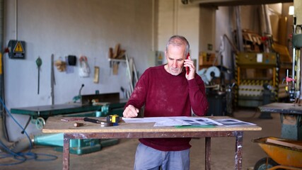 Senior woodworker managing small business with phone call © Iván Moreno