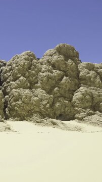 A large formation made of sand and dust rises up in the desert. The bright blue sky is clear with no clouds. The ground is dry and sandy, showing minimum vegetation.