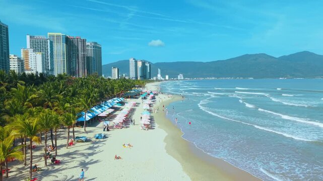 Vacation beach with palm trees and ocean waves near city skyline in Da Nang Vietnam. Vacation lifestyle concept shows summer relaxation tropical travel and seaside holiday atmosphere.