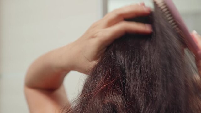 A close up view from behind of a woman with long dark brown hair. She uses a pink hairbrush to energetically brush her hair and gather it into a high ponytail. A simple daily haircare routine