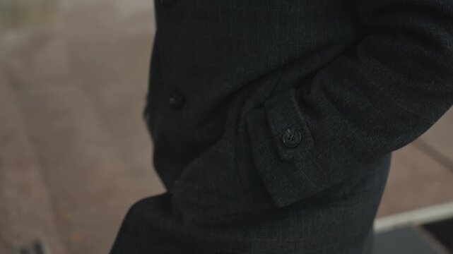 Black coat creator shifting hand pocket, close framing on cuff and buttons while stepping on city pavement, movementfocused composition captures stride and purpose, commuter mood with overcast light,