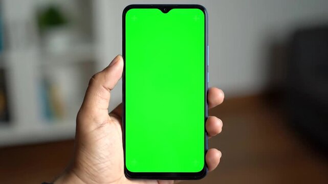 A person's hand holds a modern electronic device with a bright green screen, ready for digital content