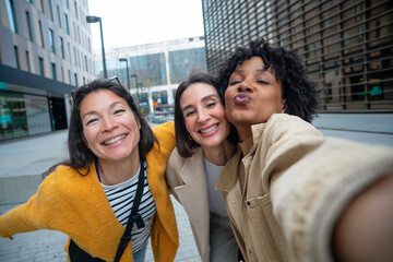 Diverse young women friends taking happy selfie in city