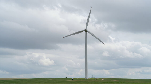 Wind turbine rotating on green field under cloudy sky.