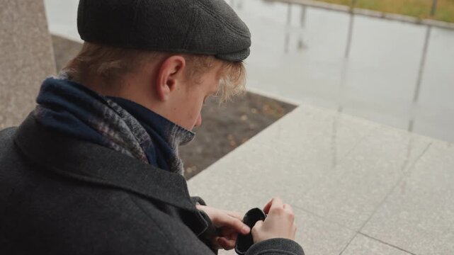 Man putting on leather gloves, coat urban granite ledge by wet pavement, beanie and scarf visible, moody cinematic closeups of hands and texture, quiet anticipation as creator prepares for outdoor