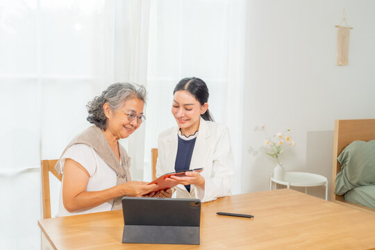 Senior woman consulting with insurance agent at home, health insurance planning and financial discussion, elderly client reviewing policy details on tablet and documents during consultation session