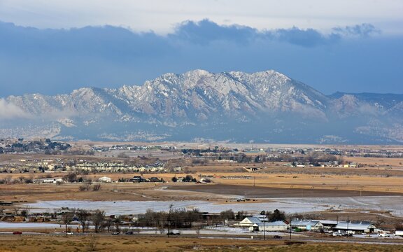 the  striking boulder flatirons and  snow -capped peaks of the front range of the colorado rocky mountains in  spring, with dramatic clouds and farm houses,  as seen from broomfield, colorado, in earl