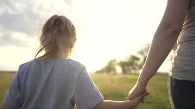 Holding child hand walking through field at golden sunset parent and child holding hand while walking across tall grass in open meadow family connection outdoors warm sunlight and gentle breeze