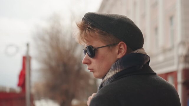 Chic street explorer with vintage style analyzes skyline scenery thoughtfully. Stylish individual with sunglasses gazes over city skyline capturing architectural details with artistic intent