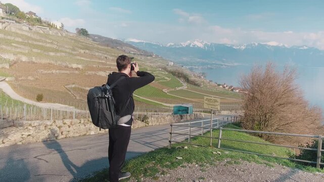 Male photographer taking pictures in Lavaux during the day with Lake Geneva and mountains in Canton of Vaud, Switzerland, static shot
