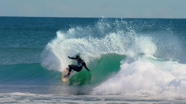 Surfer performing aerial maneuver, cutting back to spray with deep lean on bright turquoise ocean wave, slow motion
