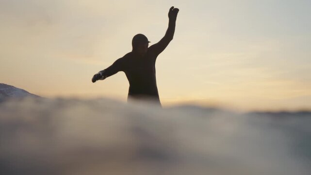 Surfer balancing on small wave near snowy mountains at sunset, longboard style walking under yellow sky