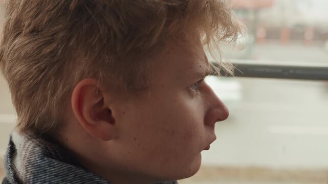 Young man by window overlooking street, creator sketching ideas in head, profile closeup with scarf, passing cars blurred through glass, damp pavement, subdued light, reflective mood, urban narrative