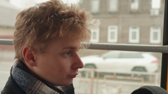 Young white creator on commute staring out rainy window, wrapped in plaid scarf and coat, removing flat cap and rubbing eyes quiet reflective mood, roles shift between writer, poet, and student