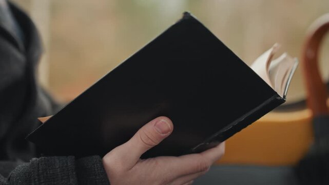 Hands holding black notebook on bus, creator jotting notes and sketches, closeup of leather cover and yellow seatback, soft autumn light through window, quiet reflective mood and steady page turn