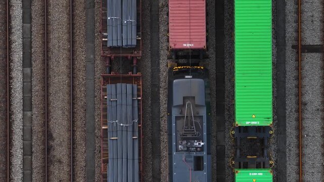 Aerial view of train cars with pipes and containers in contrasting colors, awaiting transport on parallel tracks, Lisbon, Portugal.