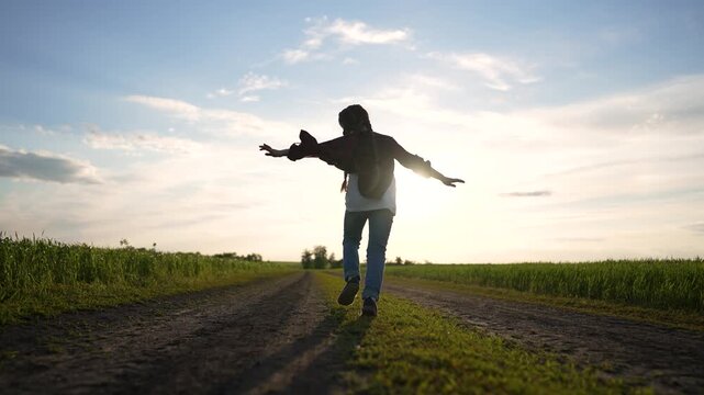 Girl running on country road at sunset, silhouette against wide sky and golden grass, joyful movement and freedom across open field, casual jacket and braid, playful stride toward distant horizon