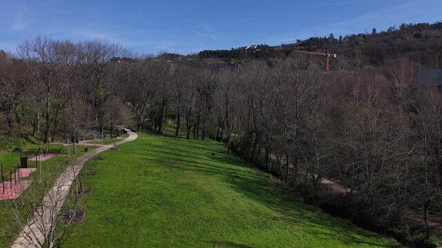Aerial view of a park featuring vibrant green grass, a winding path, and bare trees casting long shadows, Guimaraes, Portugal.