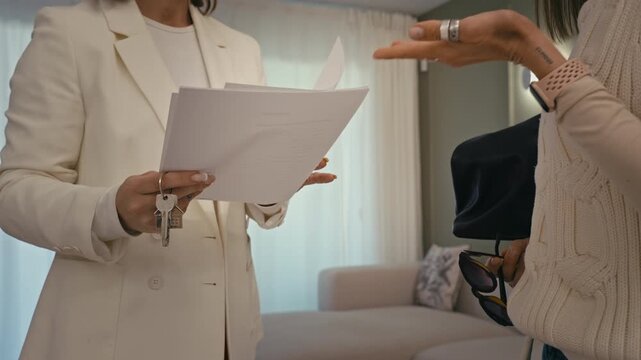 Professional real estate agent hold keys and contract, explain terms of lease agreement to female client before signing paperwork in new apartment.Property deal completion and ownership concept.