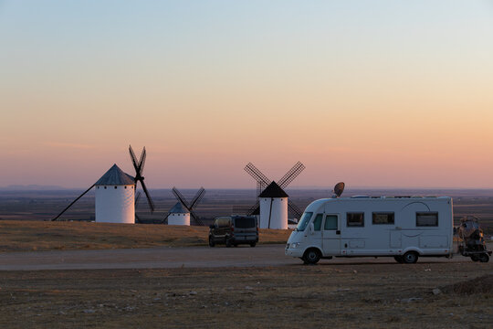 Camper van traveling past windmills at sunset in Campo de Criptana